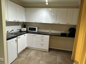 Compact kitchen with modern design, featuring white cabinetry, black countertop, and stainless steel sink.