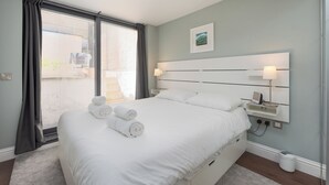 Quarto moderno com uma cama grande, duas luminárias de cabeceira, uma mesinha de noite e vista para o exterior por uma porta deslizante.