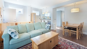 Uma sala de estar moderna com um sofá azul claro, mesa de centro de madeira e uma área de jantar com mesa e cadeiras de madeira.