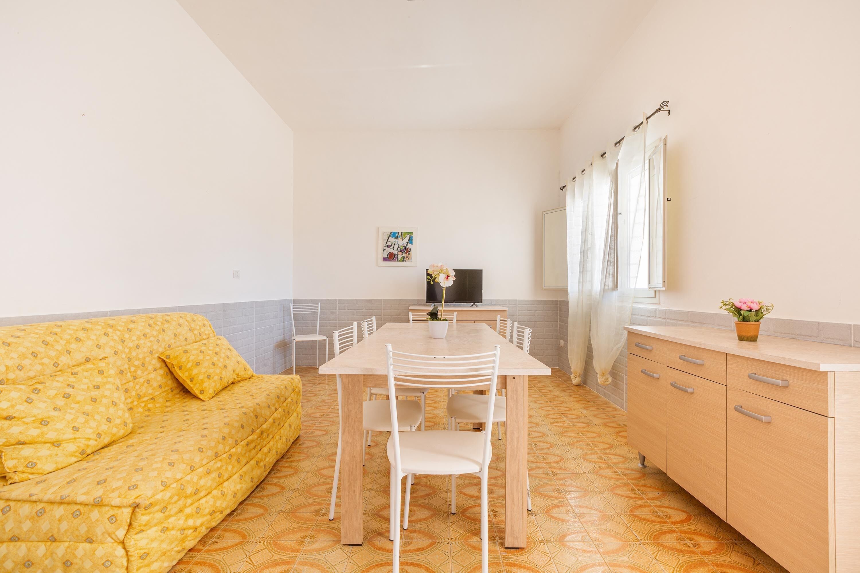 A compact living space with a sofa, a dining table with chairs, a TV, and a kitchen area with cabinets and a countertop.