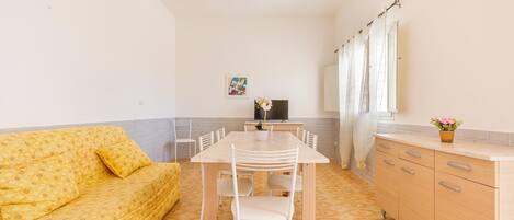 A compact living space with a sofa, a dining table with chairs, a TV, and a kitchen area with cabinets and a countertop.