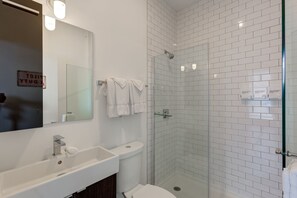 Features a large sink, glass shower enclosure, and toilet, along with a mirror and towel.