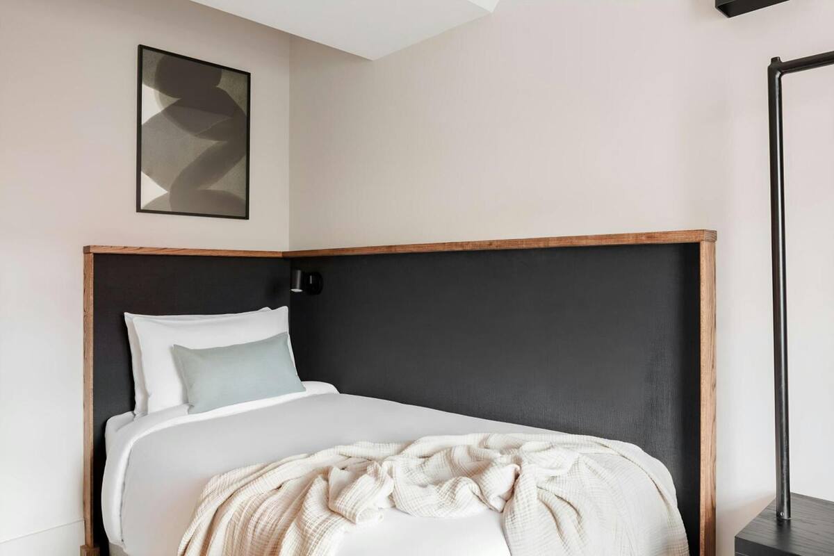 Una cama bien tendida con un cabecero de madera, una manta de color claro y una almohada.