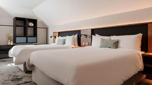 Una habitación de hotel moderna con dos camas, una estantería empotrada y un gran ventanal que ofrece luz natural.