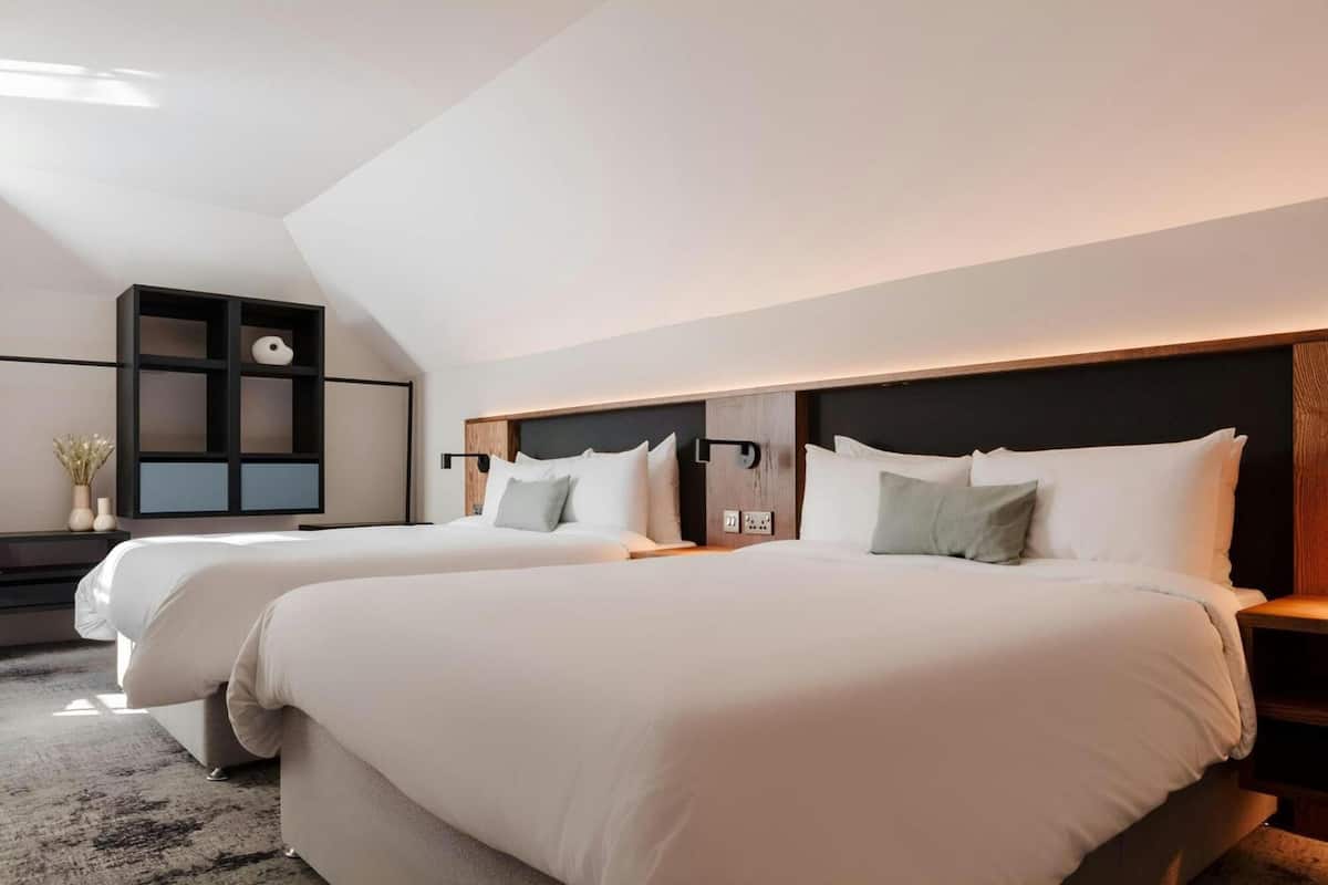 Una habitación de hotel moderna con dos camas, una estantería empotrada y un gran ventanal que ofrece luz natural.