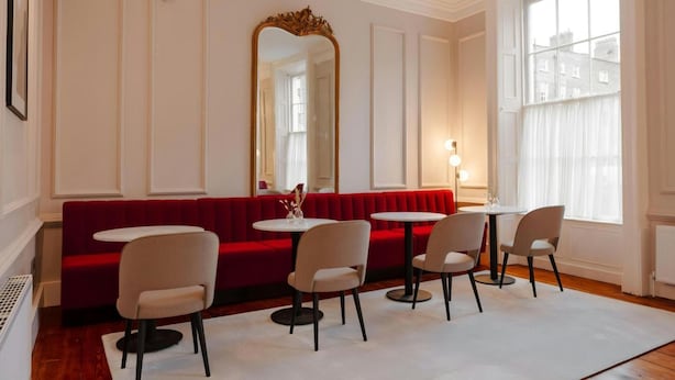 Una habitación con un banco tapizado en rojo, cuatro sillas, una mesa redonda y un espejo grande.