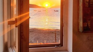 Een kamer met een raam dat uitkijkt op een zonsondergang boven het water.