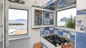 Een keuken met uitzicht op zee, een raam met uitzicht op een boot, en een plank met keukengerei.
