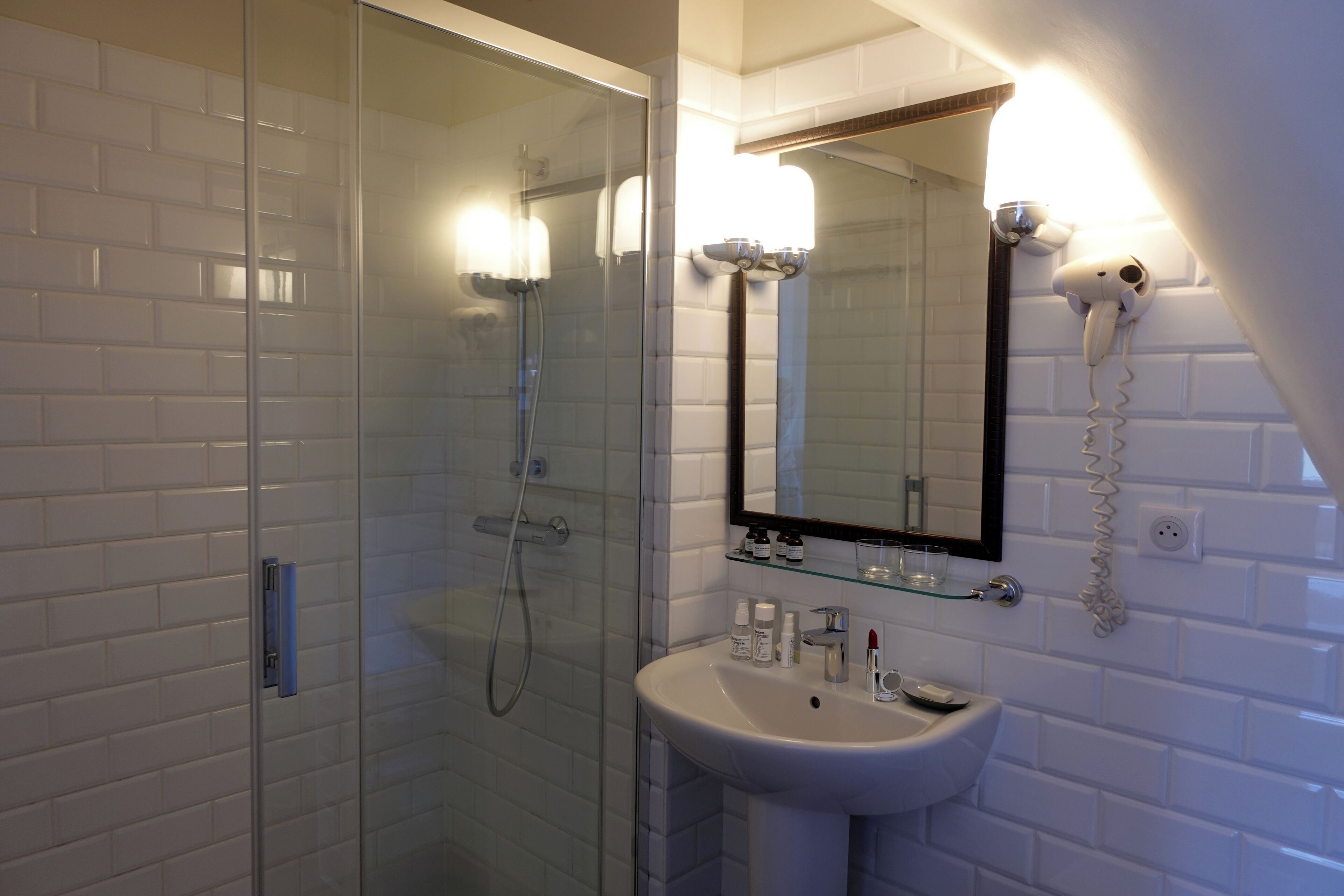 Un bany amb dutxa amb envà, un lavabo blanc i un mirall amb un assecador de cabells fixat a la paret.