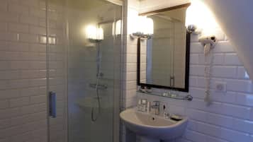 Un baño con ducha envuelta en vidrio, un lavamanos blanco y un espejo con secador de pelo montado en la pared.