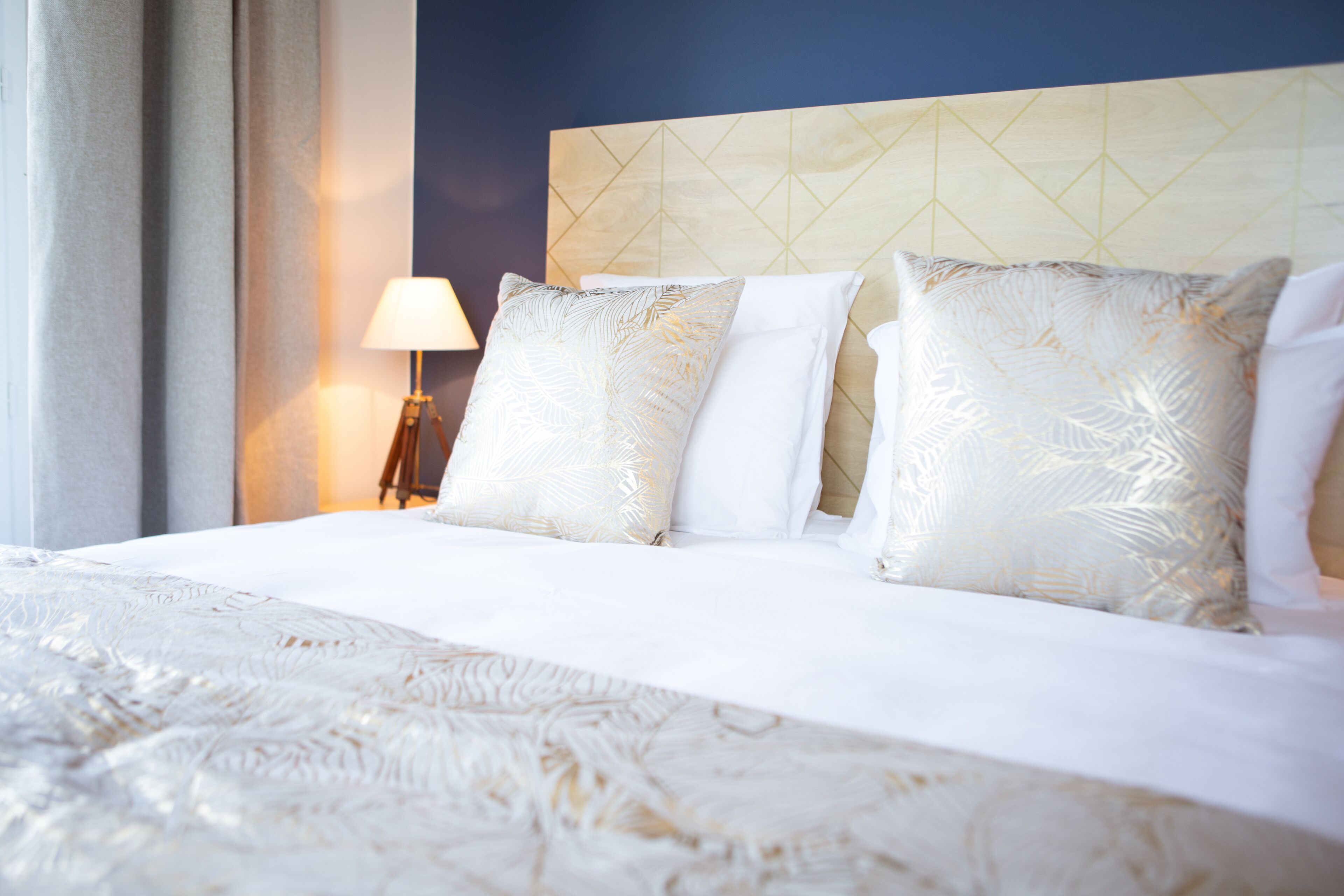 A neatly made bed with patterned pillows, a bedside lamp, and a headboard with a geometric design.