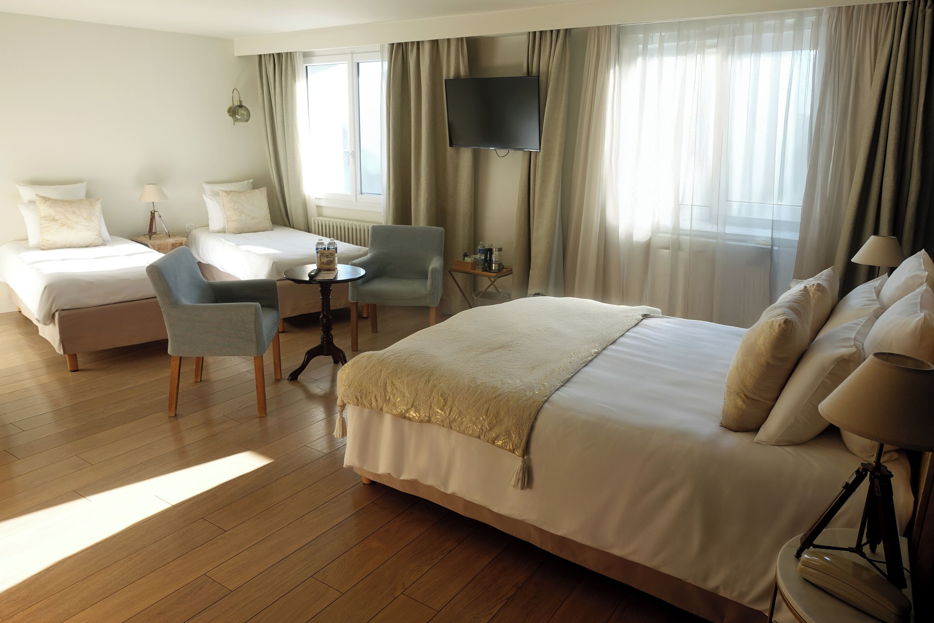 Une chambre d’hôtel avec deux lits, un bureau, une chaise, une télévision et de grandes fenêtres avec des rideaux.