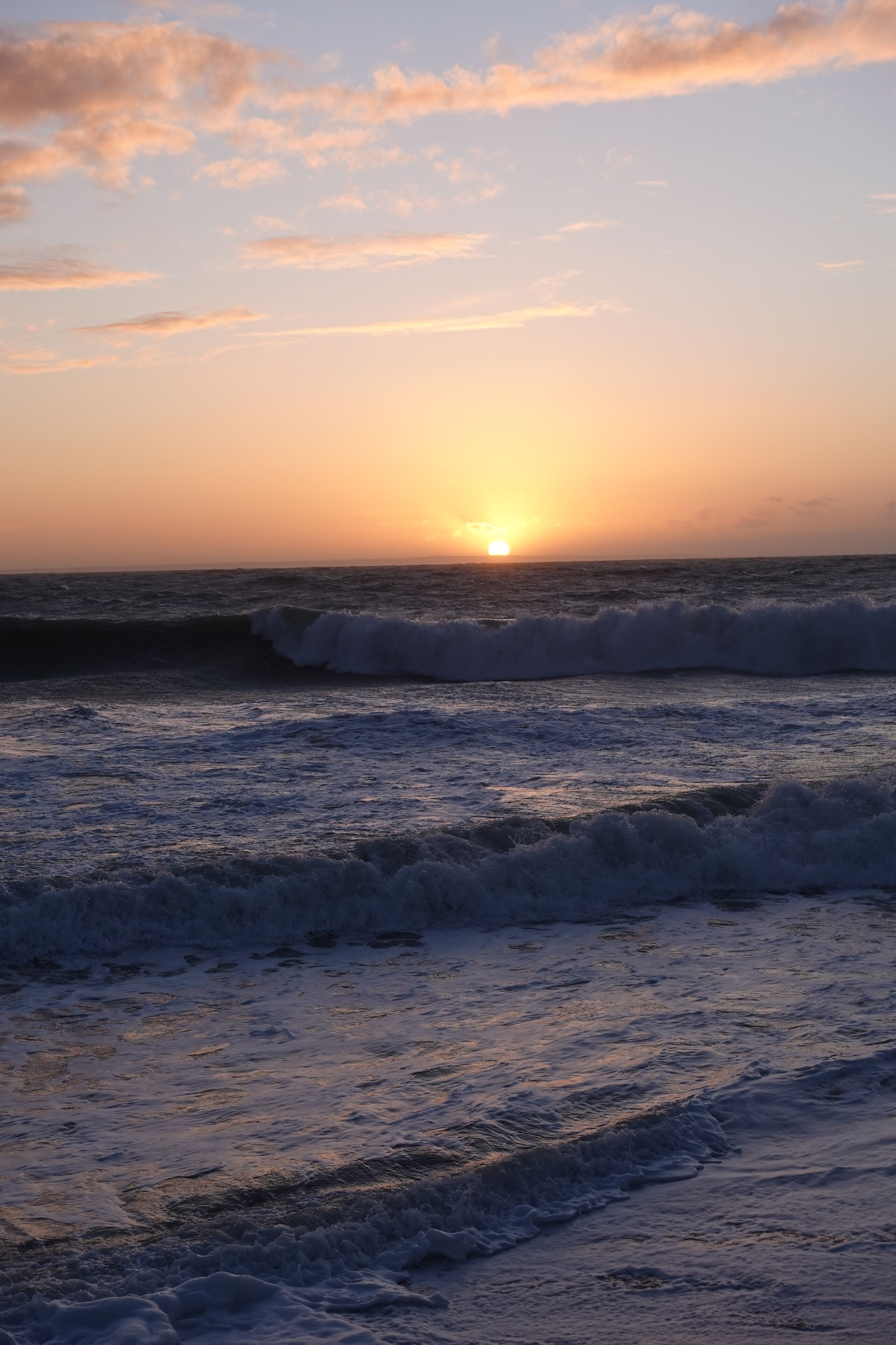 A sunset over the ocean with waves approaching the shore.