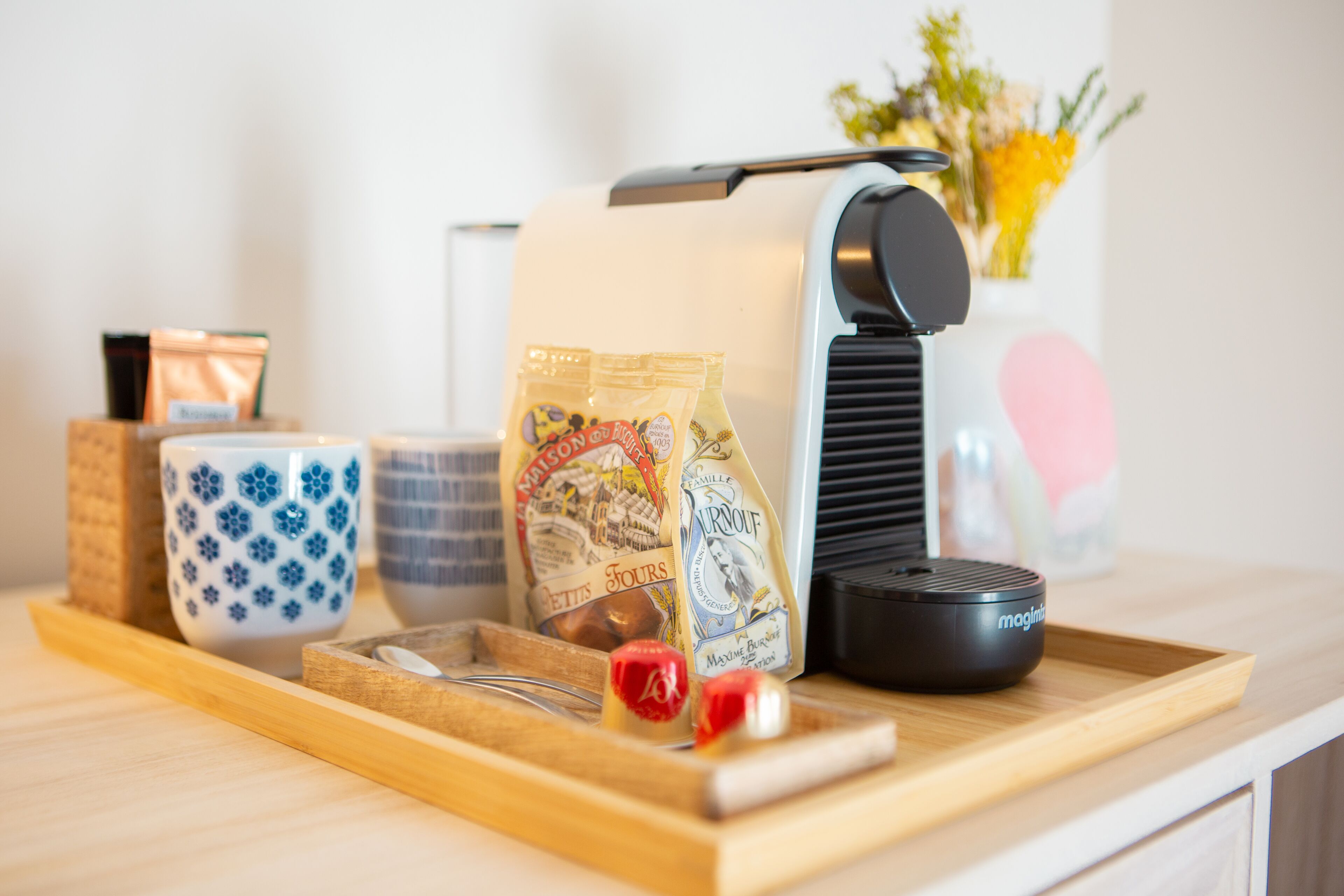 A kitchen counter with a coffee machine, a tray with a chocolate bar, a jar of jam, and a cup with a floral design.