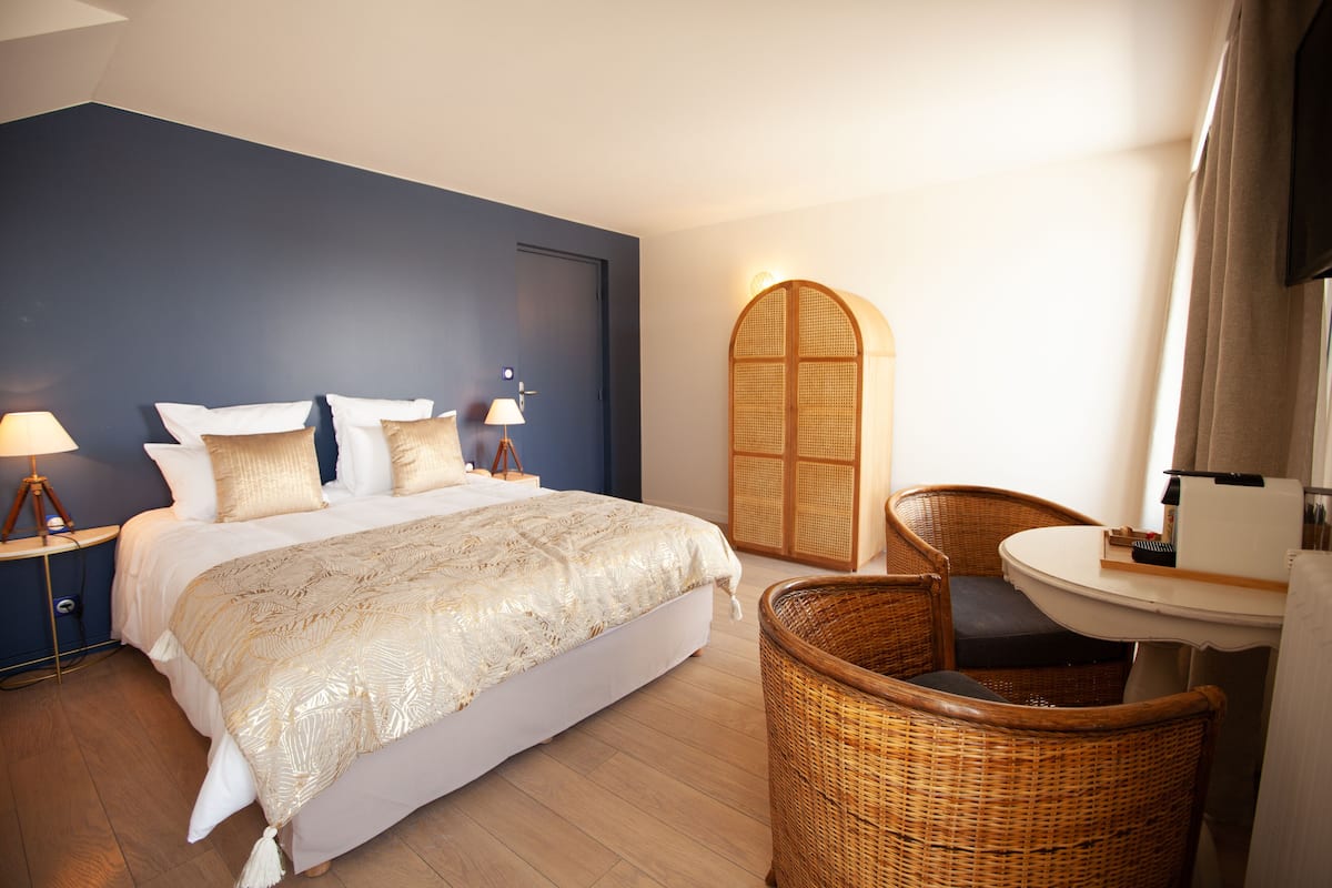 Een slaapkamer met een bed, nachtkastjes, een rieten stoel en een klein tafeltje.