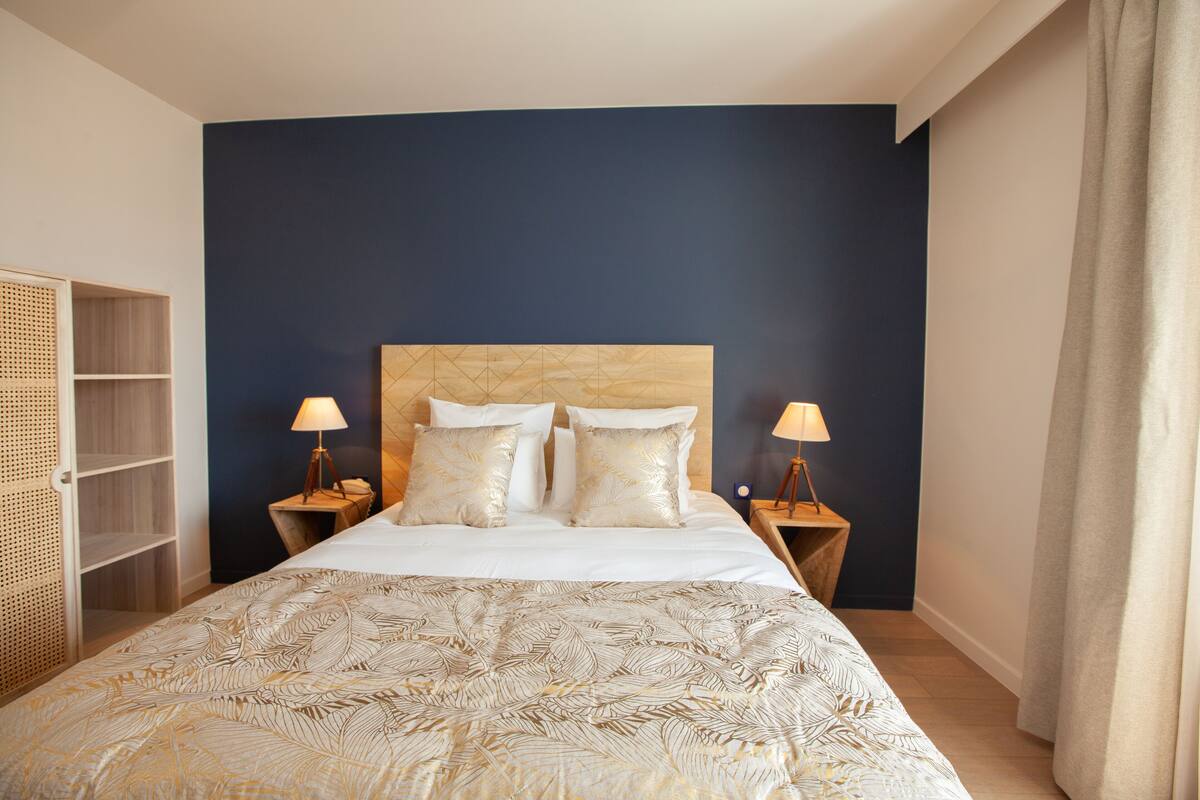 Een keurig opgemaakt bed met een bedsprei met patroon, twee bedlampen en een houten hoofdbord.