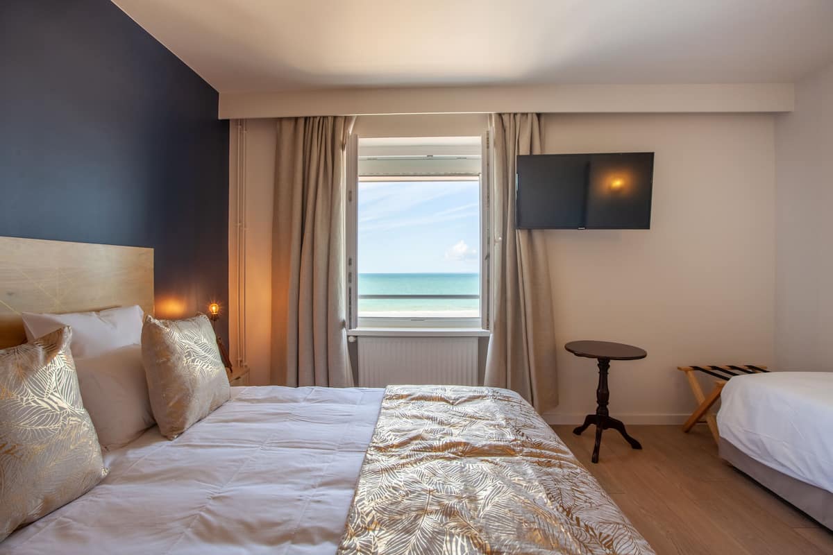 Een hotelkamer met een bed, een aan de muur bevestigde televisie, een klein tafeltje en uitzicht op de oceaan door een raam.