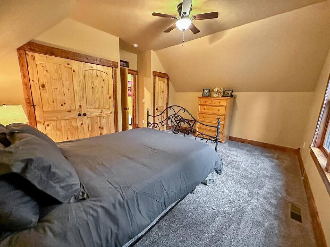 Une chambre à coucher comprenant un lit, une armoire en bois, une commode et un ventilateur de plafond.