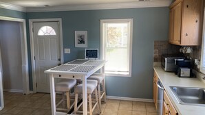 A kitchen with a white table and chairs, a window with blinds, a microwave, and a sink.
