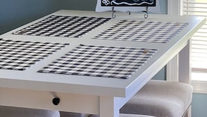 A table with a 'WELCOME GUESTS' sign, checkered placemats, and cushioned stools.