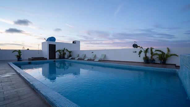 A swimming pool with a tiled edge, surrounded by lounge chairs and potted plants, set against a clear sky. - Chez Bebel with panoramic pool (Casablanca)