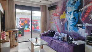 A modern living room with a purple sofa, a glass coffee table, and a mural on the wall. - Chez Bebel with panoramic pool (Casablanca)