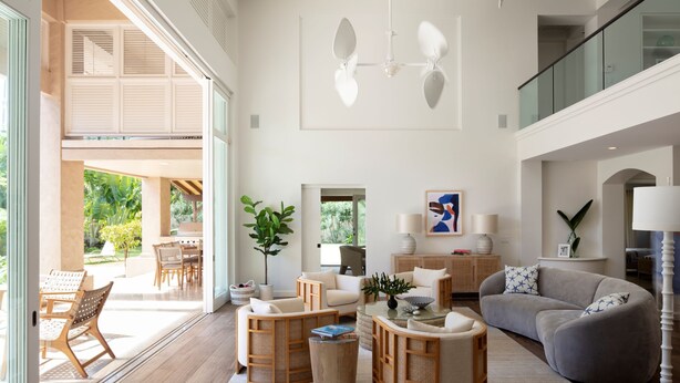 Ein geräumiges Wohnzimmer mit großem Fenster, einem grauen Sofa, einem Holztisch und einem Essbereich mit Gartenmöbeln.