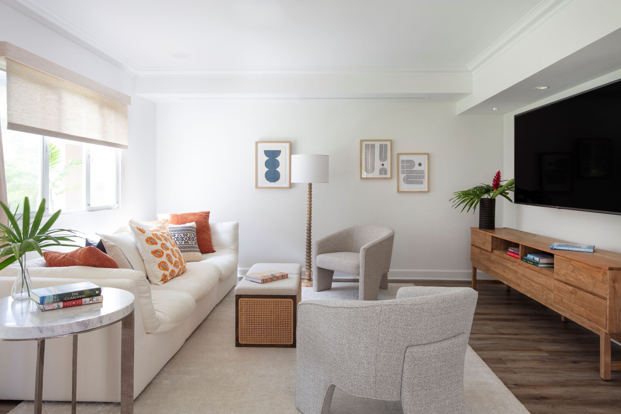 Un salon moderne avec un canapé blanc, une table basse ronde, un fauteuil gris, un meuble TV en bois et un grand téléviseur à écran plat.