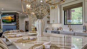 A modern kitchen with a large island, white cabinetry, and a decorative vase with branches. - Summit Trails Mansion - Luxury Cabin with Views! (Sevierville)