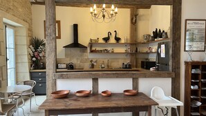 Una cocina rústica con una mesa de madera, una araña y estantes con utensilios de cocina.