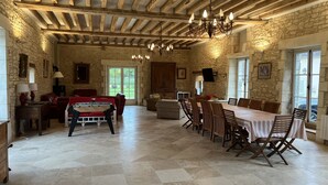 Una habitación amplia con mesa de billar, comedor con sillas, paredes de piedra, vigas de madera y una araña.