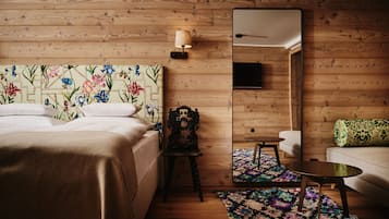 Habitación de hotel con pared de madera, cama con cabecera floral, una mesita, un sofá y un espejo.