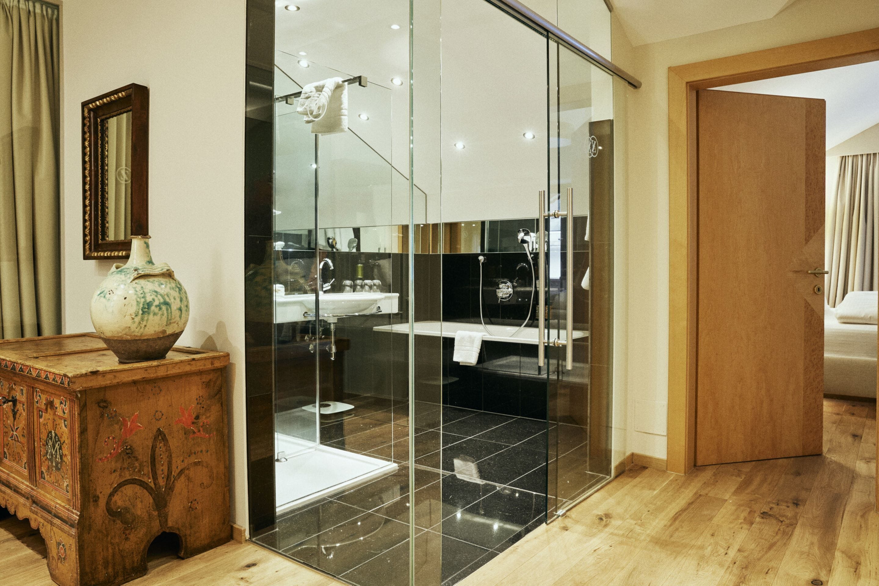 A modern bathroom with a glass shower enclosure, a wooden dresser, and a mirror on the wall.