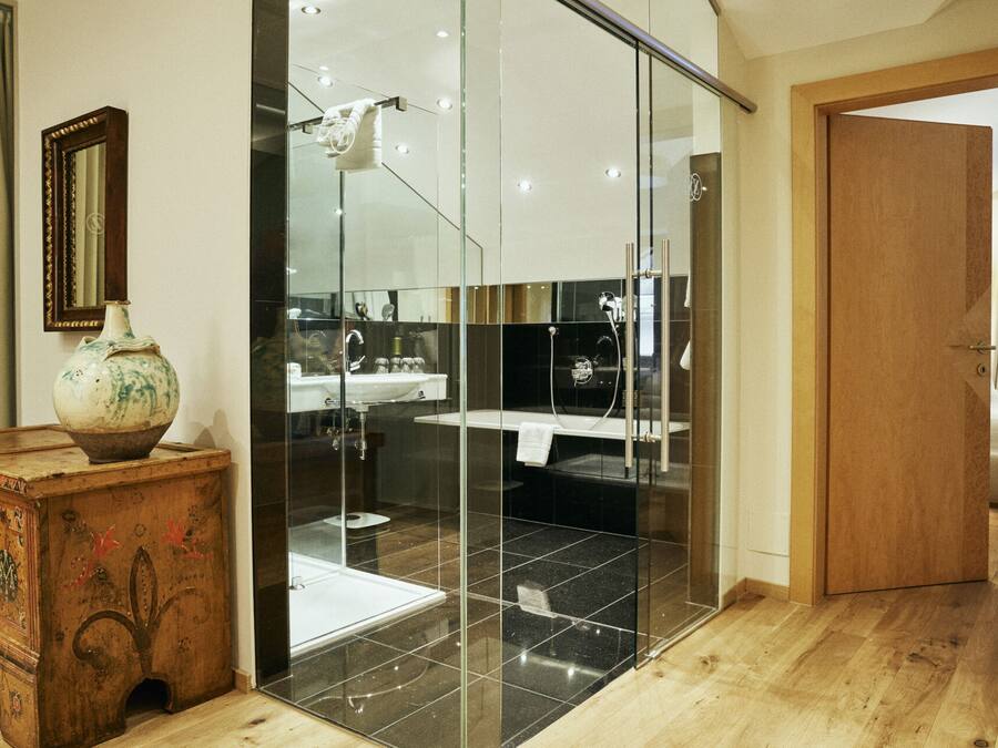 A modern bathroom with a glass shower enclosure, a wooden dresser, and a mirror on the wall.