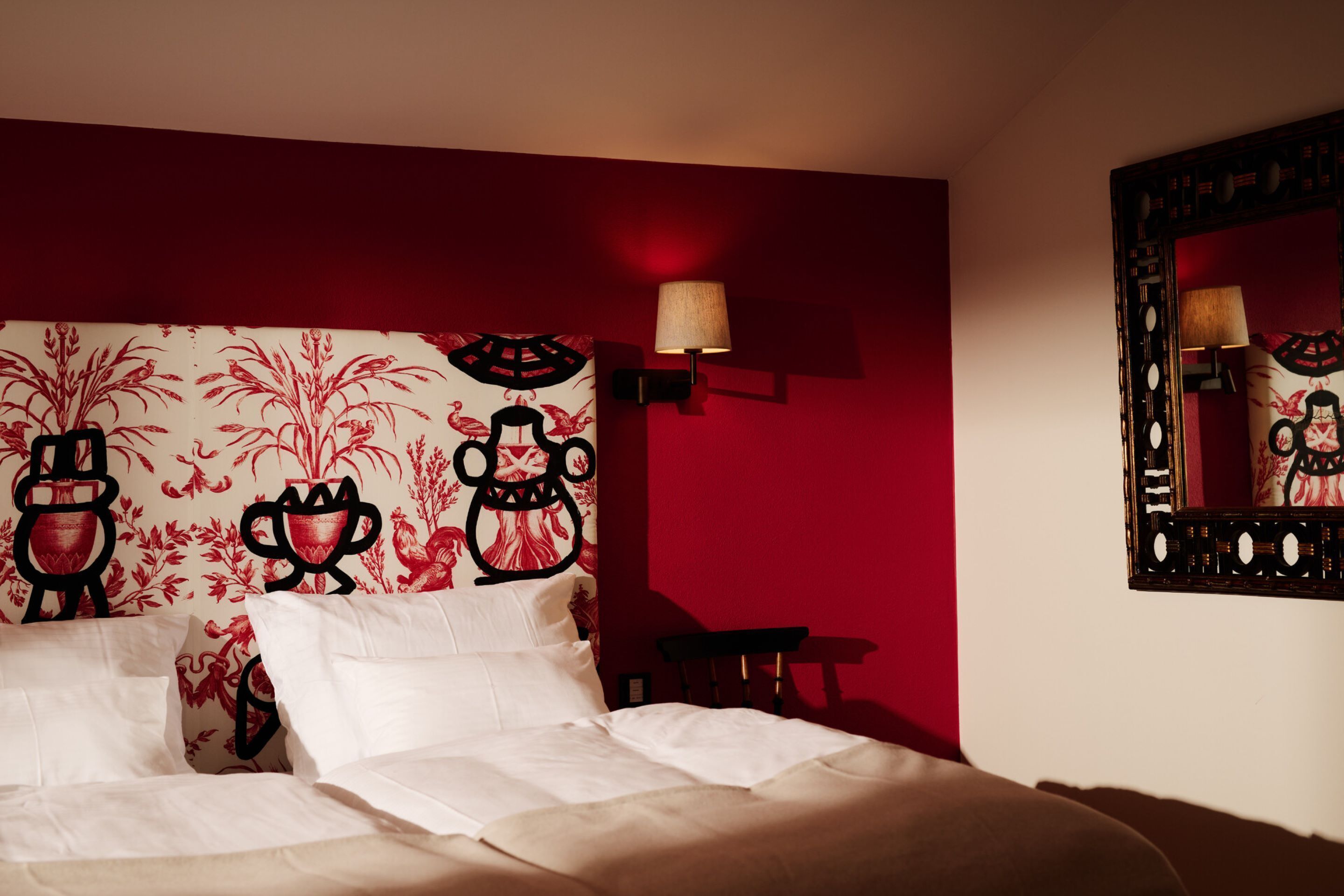 A hotel room with a bed, a wall-mounted lamp, and a mirror.