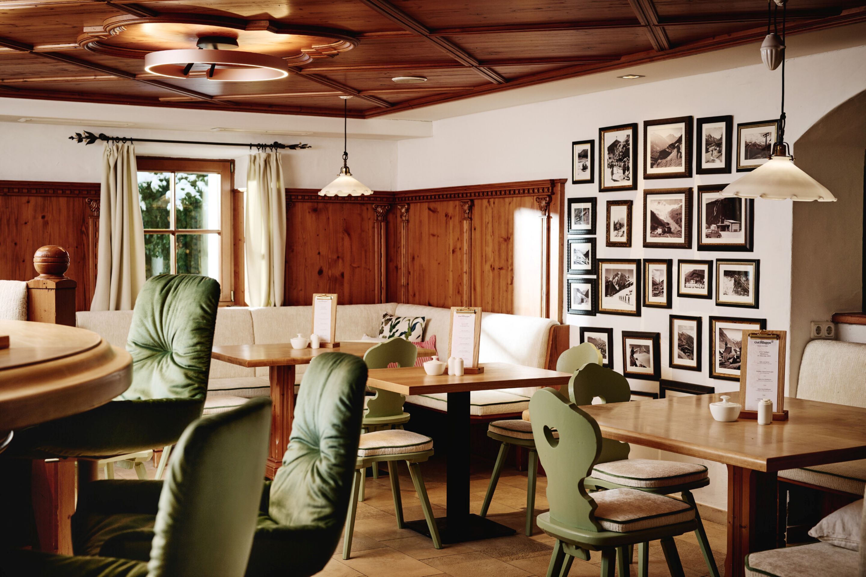 A dining area with wooden tables and chairs, a wooden ceiling, and framed pictures on the wall.