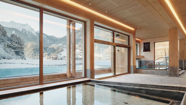 Una piscina interior moderna con grandes ventanales que ofrecen vistas a un paisaje montañoso nevado.