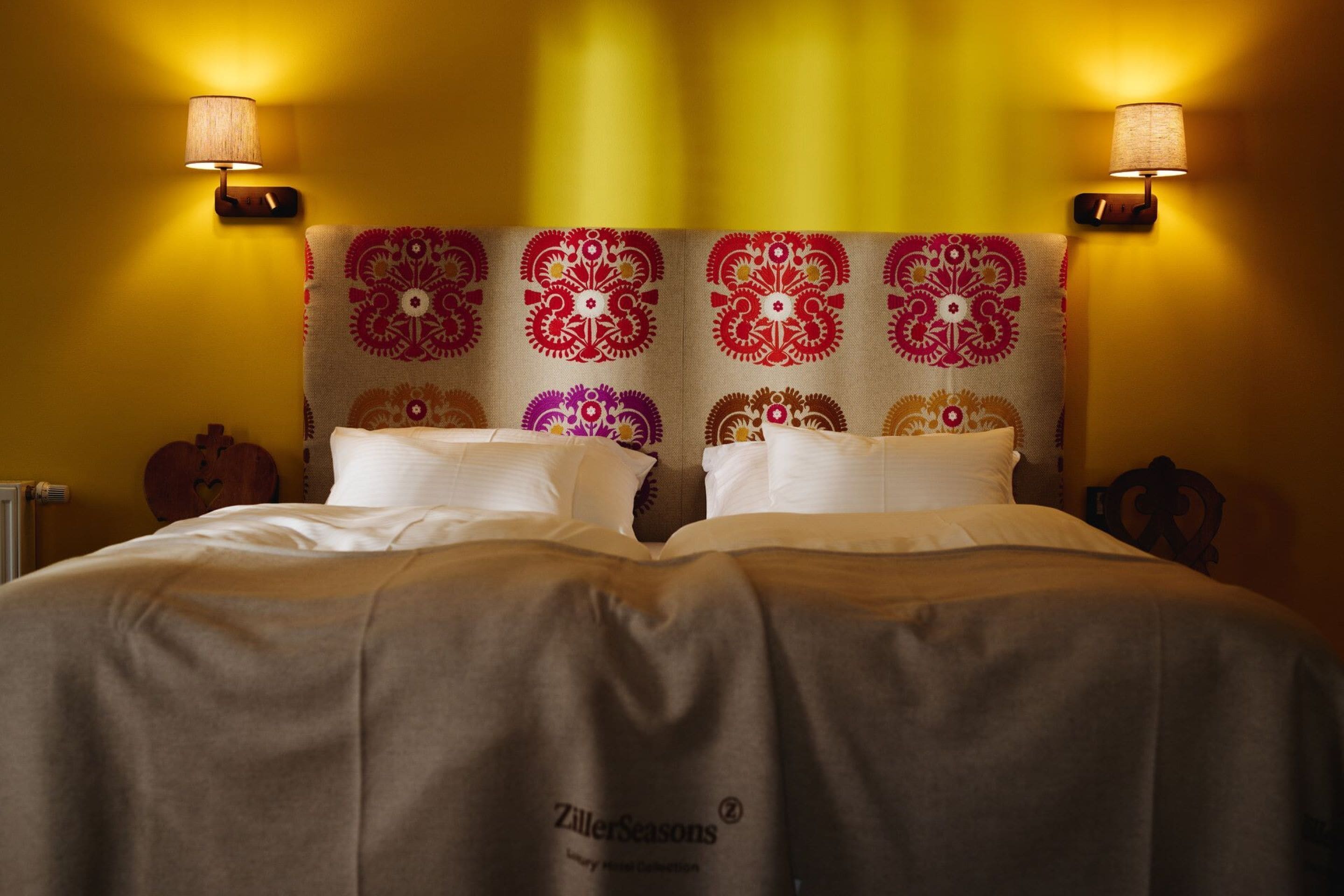A bed with a patterned headboard, two wall-mounted lamps, and a bedspread with a logo.