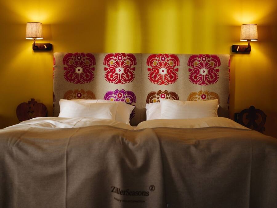 A bed with a patterned headboard, two wall-mounted lamps, and a bedspread with a logo.