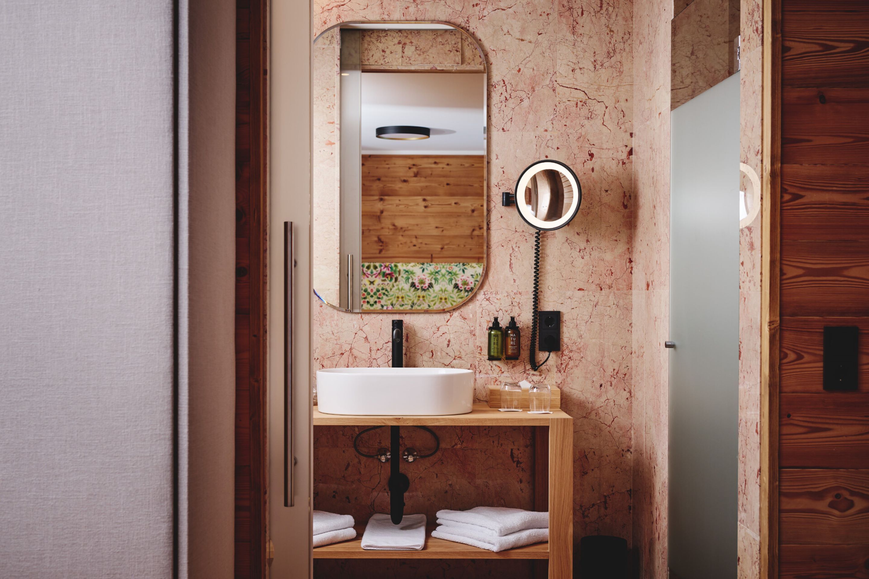 A bathroom with a wooden vanity, a white sink, a mirror, and a ring light.