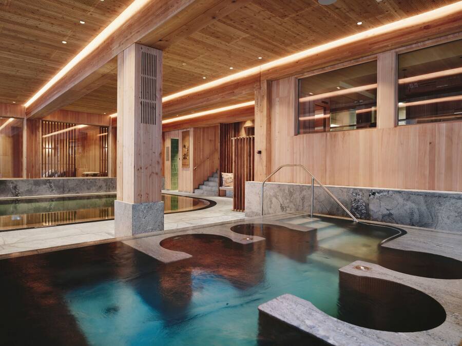 Piscina interior moderna com paredes de madeira e chão de pedra, apresentando um design geométrico único.
