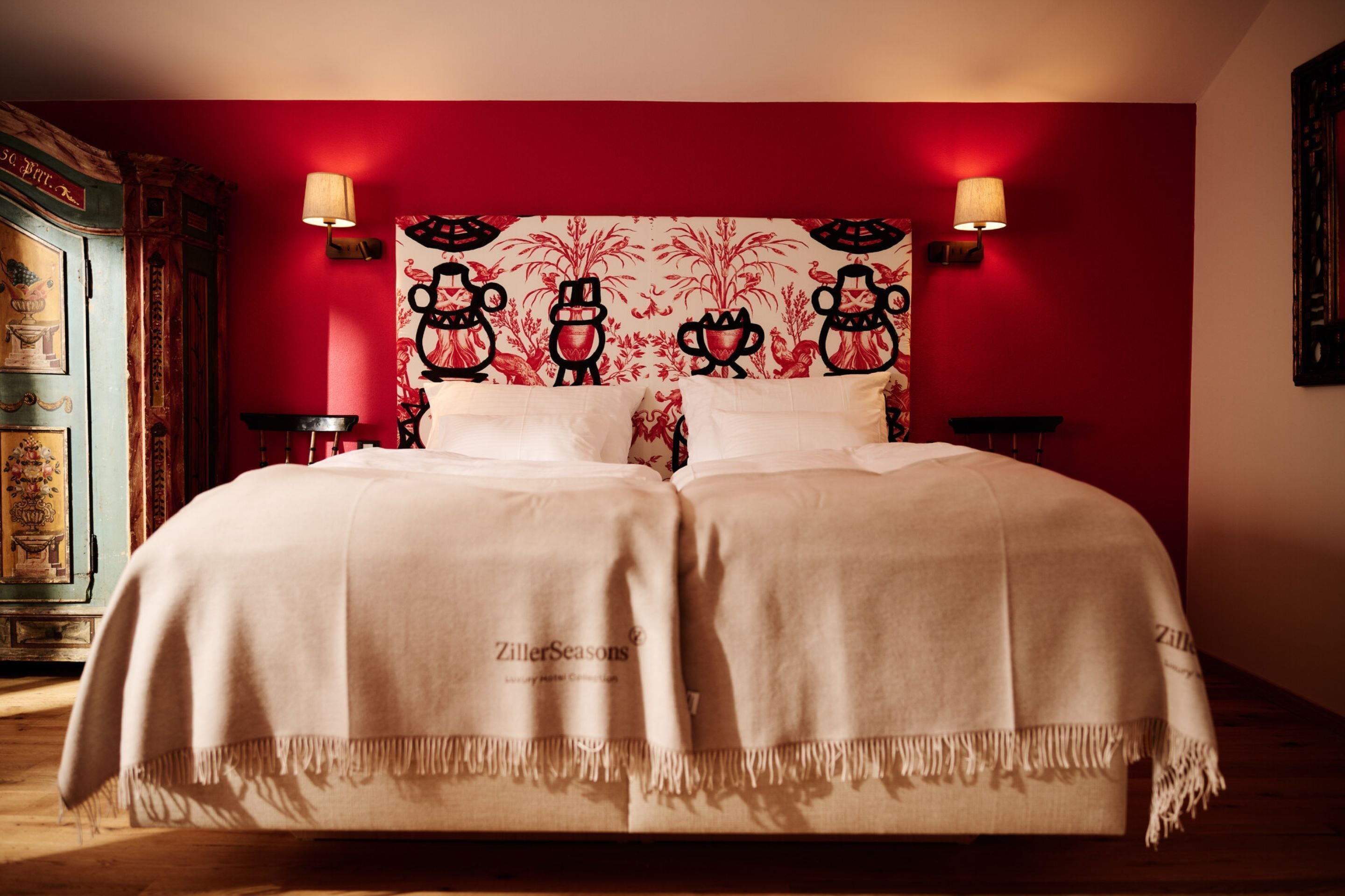 Una cama doble con cabecera estampada con motivos florales, dos mesitas de noche y una pared de acento roja.