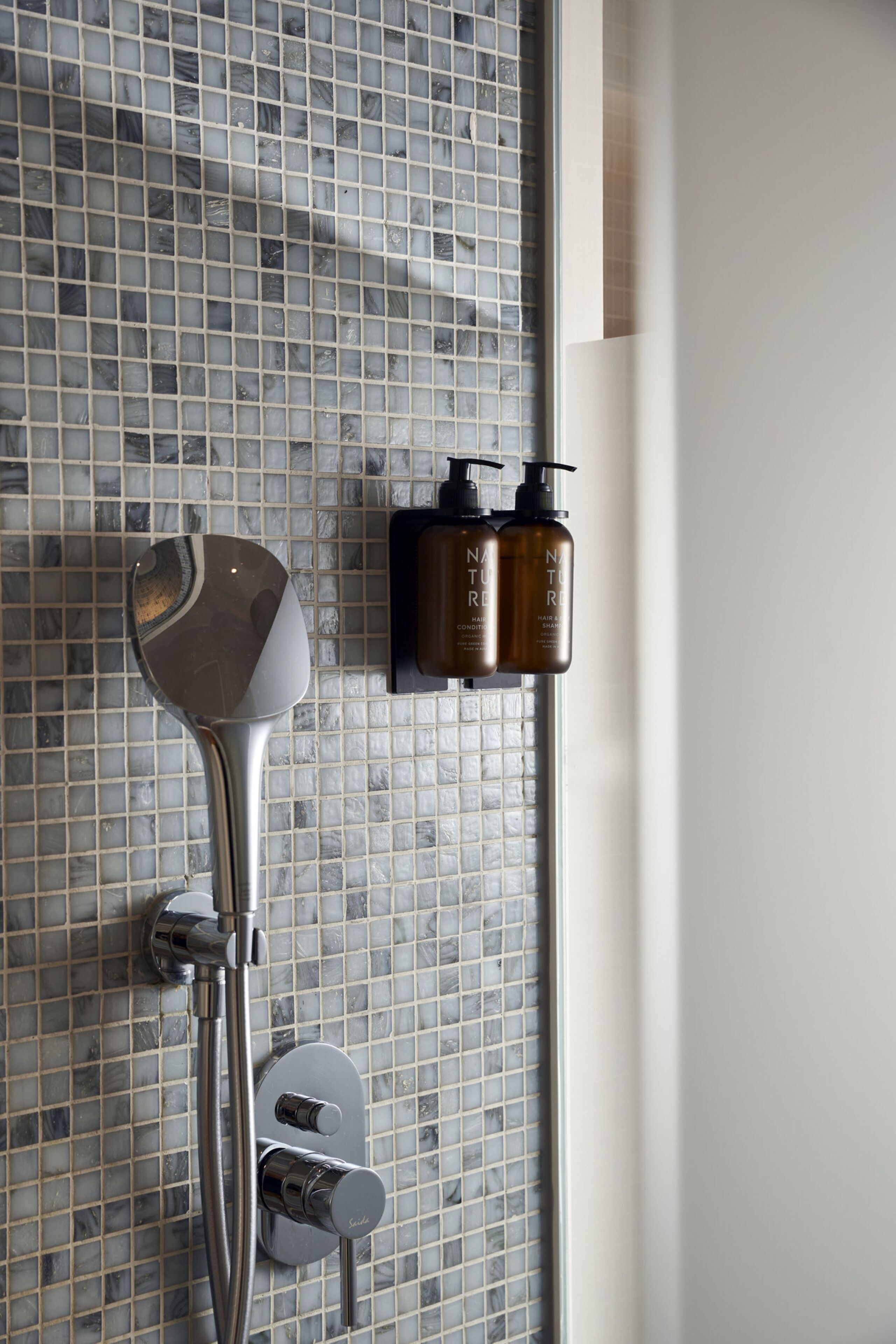Un baño con cabina de ducha de vidrio, un cabezal de ducha manual y dos botellas de champú.