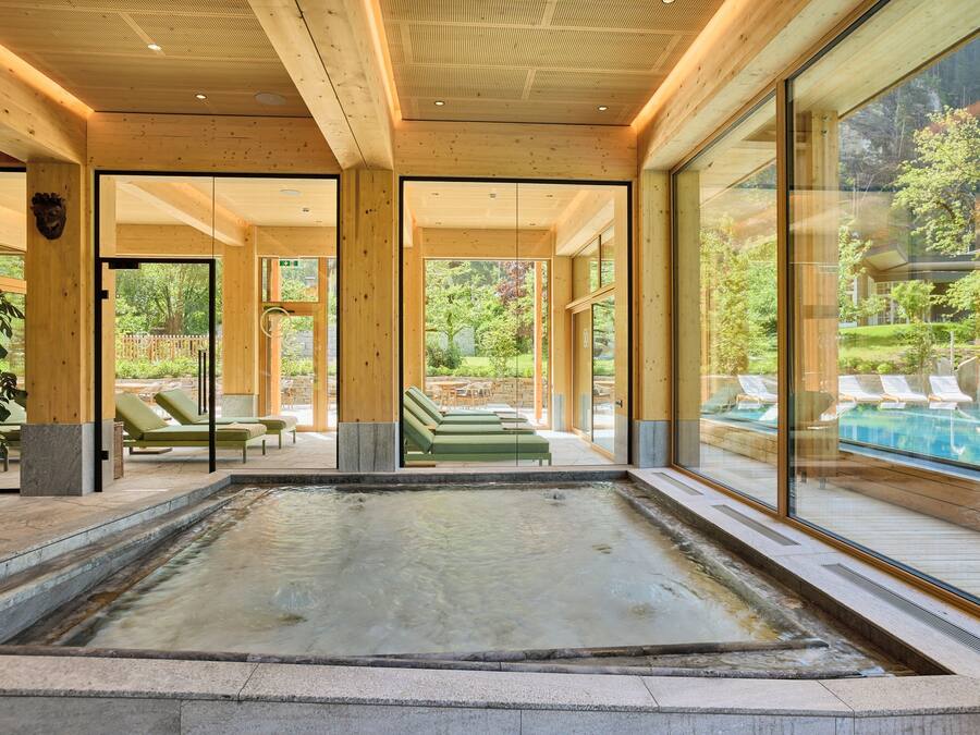 A spa area with a hot tub, lounge chairs, and a view of a pool and garden.