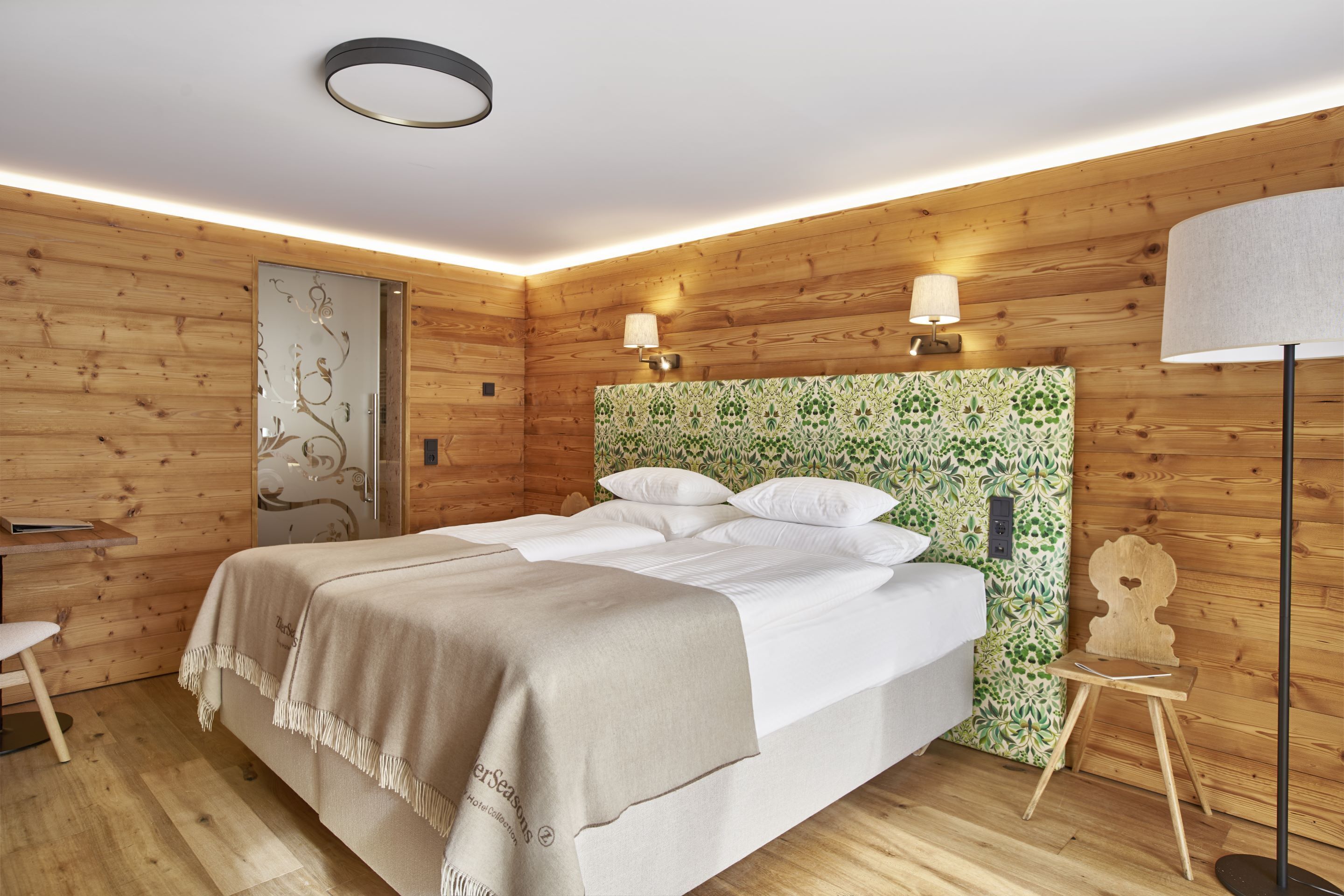 Una habitación de madera con una cama, dos lámparas de pared, una mesita y una silla.