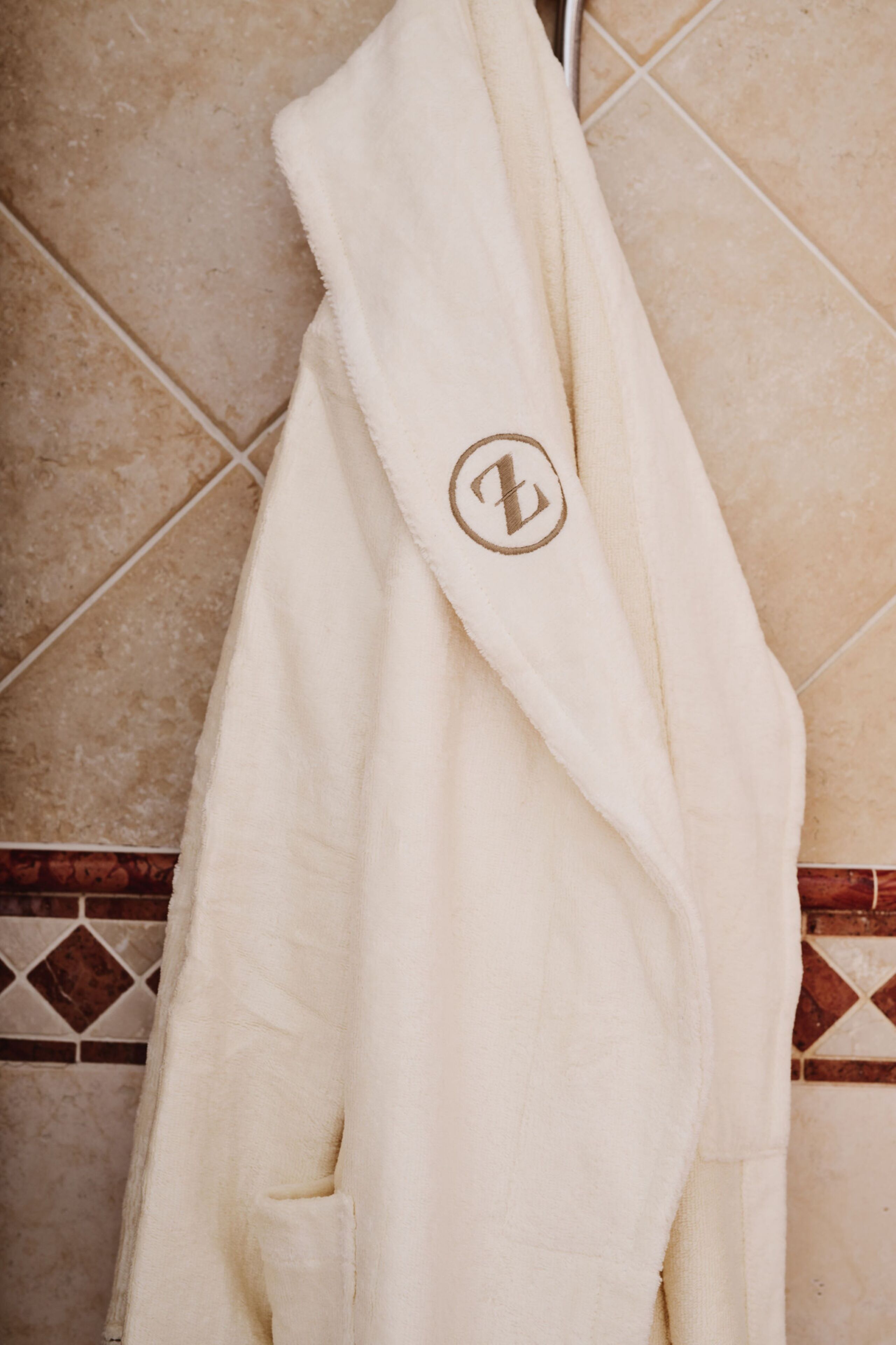 A white robe with a logo hanging on a tiled wall.