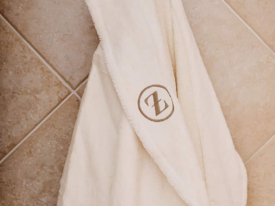 A white robe with a logo hanging on a tiled wall.