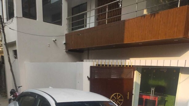 Un coche blanco estacionado frente a un edificio con balcón de madera y puerta roja.