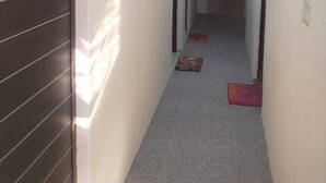 Un pasillo estrecho con una puerta de madera oscura a la izquierda y una pared de color claro. Decoraciones colgantes y coloridas se observan sobre la puerta.