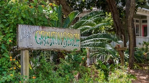 A wooden sign with "WELCOME TO GRYNY BEACH" written on it, surrounded by lush greenery and palm trees.